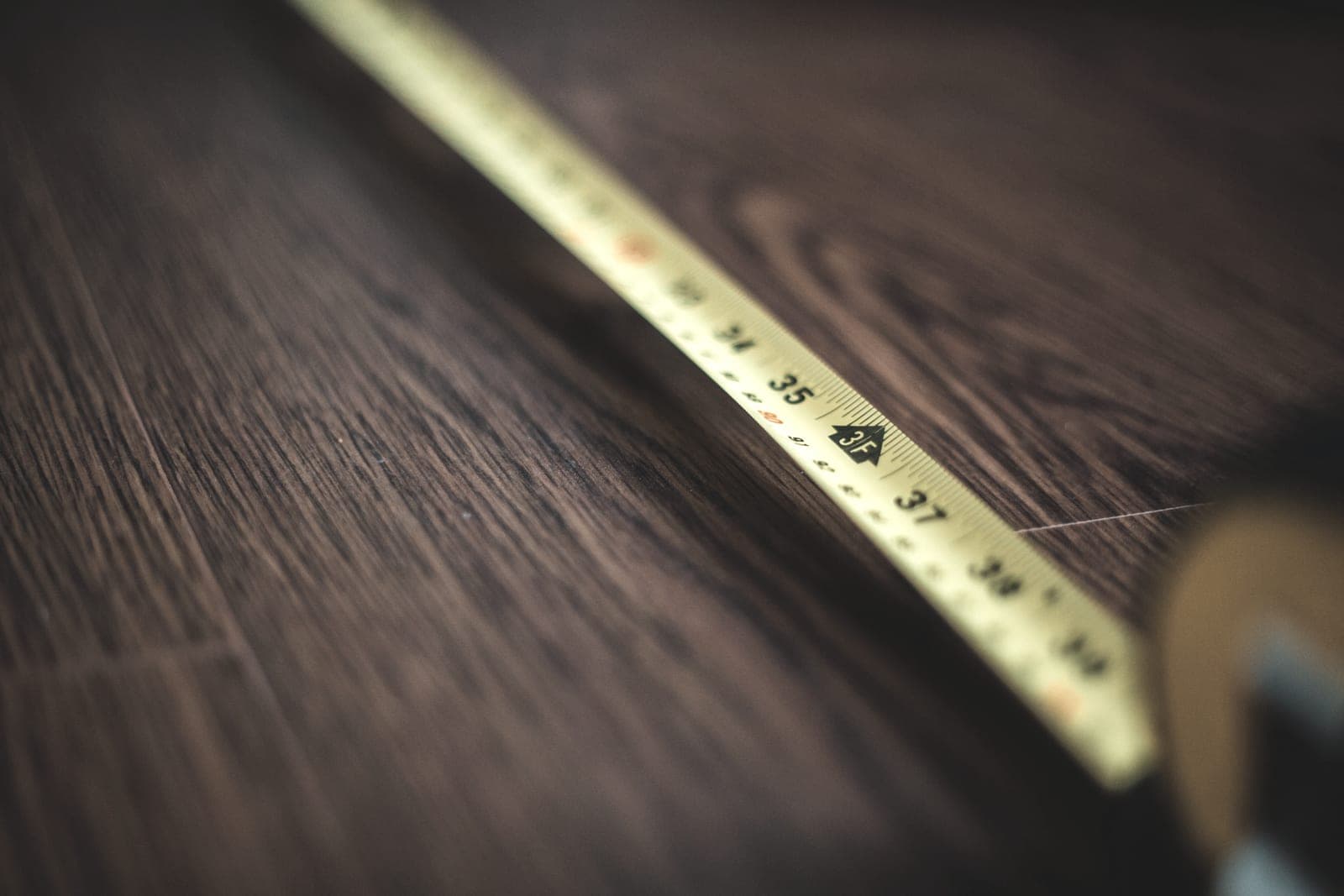 A retractable tape measure lying on a pale wooden floor